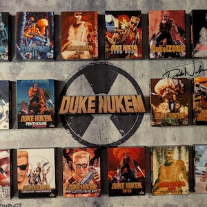 May include: A collection of Duke Nukem video game box art, featuring various action-packed illustrations. The boxes display the game's logo and character in dynamic poses, with vibrant colors and retro graphics. The collection includes titles like "Duke Nukem 3D" and "Duke Nukem Forever".