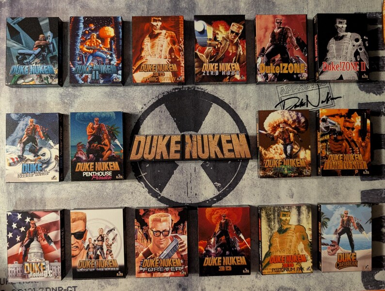May include: A collection of Duke Nukem video game box art, featuring various action-packed illustrations. The boxes display the game's logo and character in dynamic poses, with vibrant colors and retro graphics. The collection includes titles like "Duke Nukem 3D" and "Duke Nukem Forever".