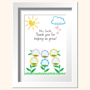 May include: A framed print with a white border features a colorful, hand-drawn design. The artwork includes a yellow sun, a blue cloud with the text "2025-2026", and six flowers in various colors. The text reads, "Mrs. Smith, Thank you for helping us grow!"
