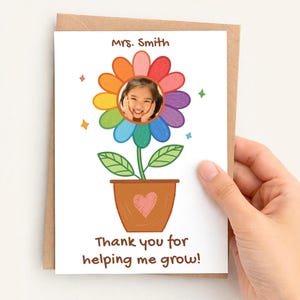 May include: A greeting card featuring a colorful flower design with a child's photo in the center. The flower has rainbow-colored petals and is in a brown pot with a heart. Text reads "Mrs. Smith" and "Thank you for helping me grow!"