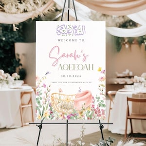 Op de afbeelding: Een welkomstbord voor Sarah's Aqeeqah, met bloemenillustraties en een babywieg. Het bord bevat Arabische kalligrafie en de datum 30.10.2024, met de tekst "Welkom bij Sarah's Aqeeqah" in een scriptlettertype. Het bord wordt op een zwart schildersezel weergegeven.