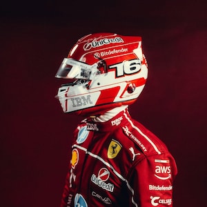 May include: A red and white racing helmet with the number 16, and sponsor logos including UniCredit, Bitdefender, and IBM. The helmet is worn with a red racing suit featuring additional logos and branding.