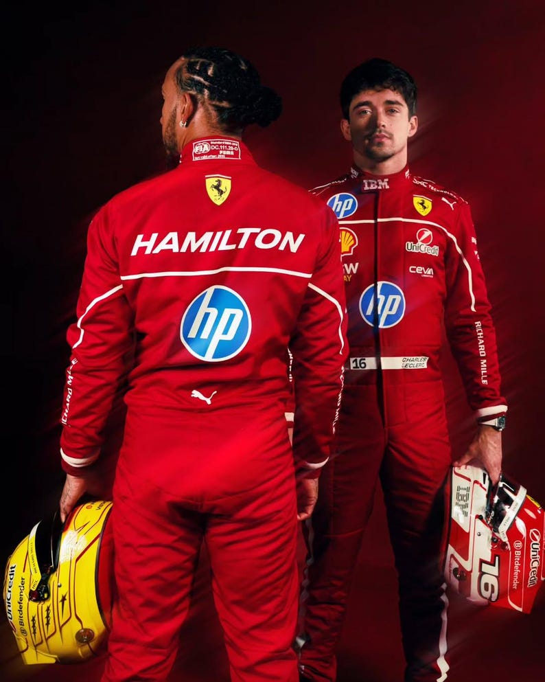 May include: Two Formula 1 racing drivers in red racing suits with white accents. One suit has "HAMILTON" printed on the back, the other has "CHARLES LECLERC" printed on the front. Both suits feature sponsor logos and the number "16". One driver holds a yellow helmet, the other a red and white helmet.