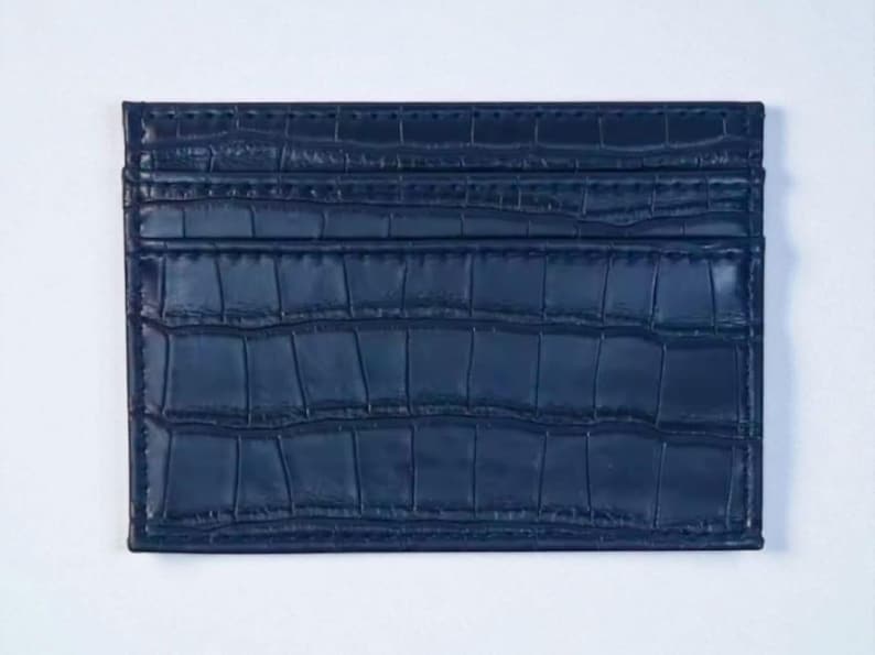 Puede incluir: Un tarjetero azul marino con un patr&oacute;n texturizado similar al de un cocodrilo. La cartera rectangular tiene m&uacute;ltiples ranuras y est&aacute; hecha de un material duradero. El tarjetero es un accesorio elegante.