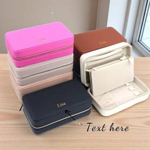 May include: A collection of personalized jewelry cases in various colors, including pink, tan, brown, and navy blue. Each case has a zipper closure and the name "Lisa" printed on the top. One case is open, revealing compartments for jewelry.