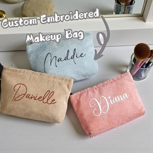 May include: Three corduroy makeup bags in light blue, peach, and tan, each embroidered with a name in a cursive font. The bags are labelled "Custom Embroidered Makeup Bag."