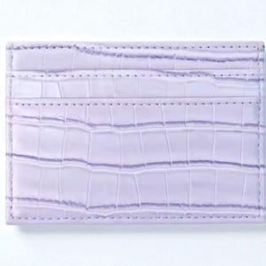 Puede incluir: Un tarjetero lavanda con textura de piel de cocodrilo. La cartera rectangular tiene tres ranuras para tarjetas y est&aacute; hecha de un material suave y duradero. Los bordes est&aacute;n cuidadosamente cosidos.