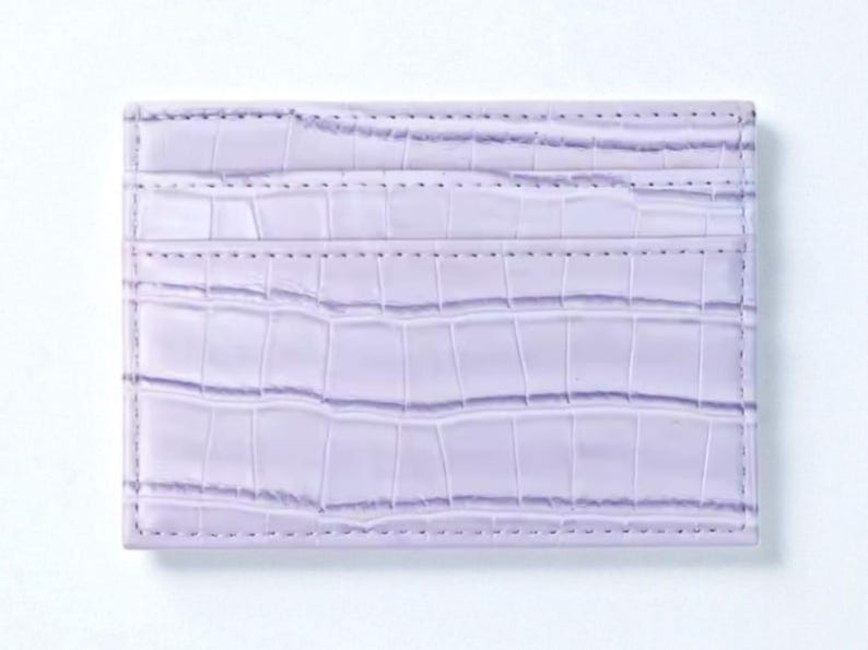Puede incluir: Un tarjetero lavanda con textura de piel de cocodrilo. La cartera rectangular tiene tres ranuras para tarjetas y est&aacute; hecha de un material suave y duradero. Los bordes est&aacute;n cuidadosamente cosidos.