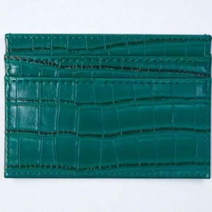 Puede incluir: Tarjetero rectangular verde esmeralda con un patr&oacute;n texturizado similar a la piel de cocodrilo. El tarjetero tiene m&uacute;ltiples ranuras y est&aacute; hecho de un material duradero. Dimensiones: aproximadamente 10 cm x 7 cm.