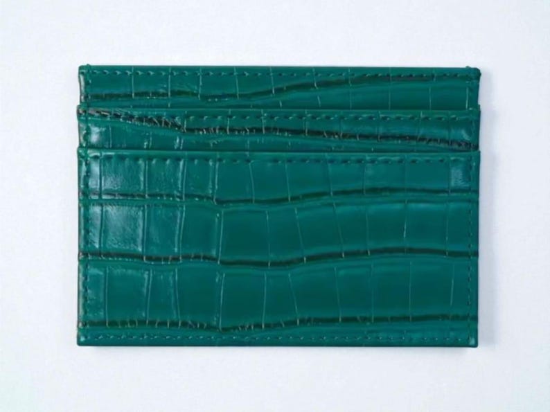 Puede incluir: Tarjetero rectangular verde esmeralda con un patr&oacute;n texturizado similar a la piel de cocodrilo. El tarjetero tiene m&uacute;ltiples ranuras y est&aacute; hecho de un material duradero. Dimensiones: aproximadamente 10 cm x 7 cm.