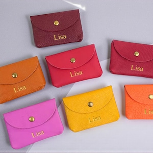 May include: A collection of small, colorful leather coin purses in shades of red, orange, yellow, and pink. Each purse has a flap closure with a gold snap and the name "Lisa" embossed on the front.