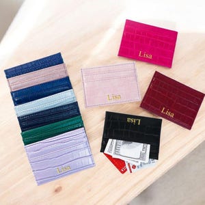 Puede incluir: Varios tarjeteros de cuero en colores como rosa, rojo, negro y azul. Cada tarjetero presenta un patr&oacute;n de cocodrilo texturizado y el nombre "Lisa" en letras doradas. Algunos tarjeteros est&aacute;n apilados, mientras que otros se muestran individualmente.