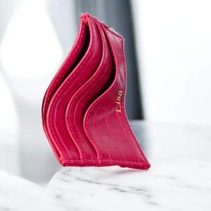 Puede incluir: Un tarjetero fucsia con un patr&oacute;n texturizado similar al de un cocodrilo. El tarjetero tiene m&uacute;ltiples ranuras y el nombre "Lisa" est&aacute; impreso en dorado. El dise&ntilde;o es elegante y moderno, perfecto para llevar tarjetas.
