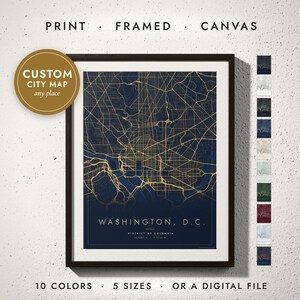 Op de afbeelding: Een ingelijste kunstdruk met een donkerblauwe kaart van Washington, D.C. met gouden straten. De tekst luidt "WASHINGTON, D.C." en "DISTRICT OF COLUMBIA" met coördinaten. Een gouden ronde badge vermeldt "CUSTOM CITY MAP".