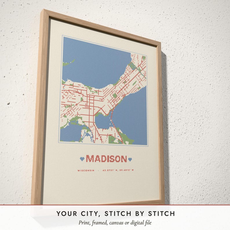 Three-quarter view of the framed Cross-Stitch City Map poster on a white plaster wall