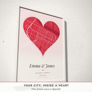 Three-quarter view of the framed Heart City Map poster on a white plaster wall