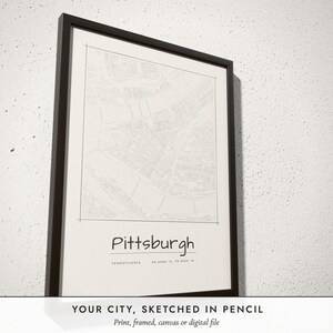 Three-quarter view of the framed Pencil Sketch City Map poster on a white plaster wall