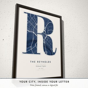 Three-quarter view of the framed Monogram Map poster on a white plaster wall