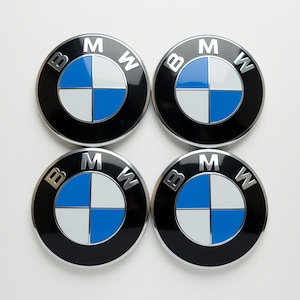 Puede incluir: Cuatro tapacubos BMW. Cada tapacubo es redondo con un borde negro, un anillo plateado y el logotipo de BMW en el centro. El logotipo presenta un diseño de cuadrante azul y blanco con las letras "BMW" en plata.