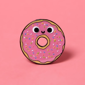 May include: A cartoon-style pink donut with a smiling face and colourful sprinkles. The donut has a light brown outline and a hole in the centre. The background is a solid pink.