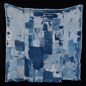 May include: A square textile piece composed of multiple rectangular fabric patches in varying shades of blue and white. The material features visible stitching, frayed edges, and a layered, distressed appearance with a patchwork construction.