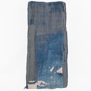 May include: A rectangular textile piece featuring a patchwork of indigo-dyed fabric with vertical pinstripes and solid blue sections. The fabric displays visible hand-stitched running lines and areas of fraying that reveal a light-colored base layer.