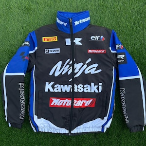 Könnte beinhalten: Schwarze und blaue Kawasaki Ninja Rennjacke mit weißen Akzenten. Sie zeigt das Kawasaki-Logo, das Wort "Ninja" in Weiß und Sponsorenlogos wie Pirelli und Motocard. Die Jacke hat einen durchgehenden Reißverschluss und einen Stehkragen.