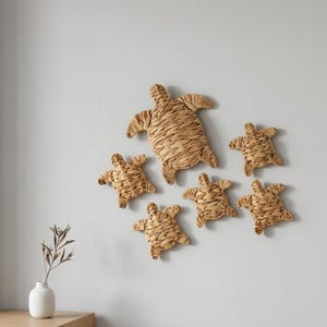 May include: A collection of six woven sea turtle wall decorations. The largest turtle is at the top, with five smaller turtles arranged below. The turtles are made of a light brown, natural-looking material and are mounted on a light gray wall.