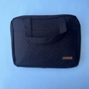 May include: Black quilted laptop sleeve with a handle. The sleeve has a geometric pattern and a gold-colored rectangular label that reads "HOTOR". The background is a light blue.
