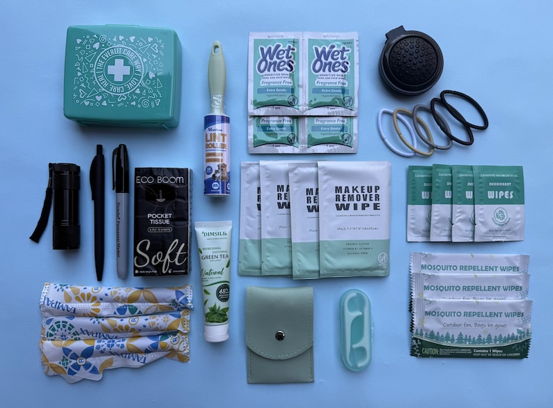 May include: An assortment of personal care items, including a first aid kit, pens, wipes, hair ties, and a lint roller, arranged on a light blue surface. The items are in various shades of green, white, and black.