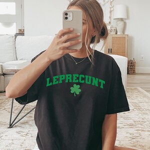 May include: Black t-shirt with the word "LEPRECONT" in green block letters and a green shamrock. The shirt is a short-sleeved, crew neck style.