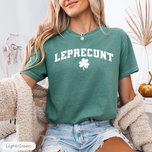 May include: Light green t-shirt with the word "LEPRECONT" in white block letters and a white shamrock. The shirt is a crew neck and has short sleeves. The shirt is made of a soft material.