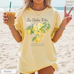 K&ouml;nnte beinhalten: Hellgelbes T-Shirt mit dem Schriftzug "La Dolce Vita" und einem Aquarell-Zitronen-Design. Der Text "Das Leben in vollen Z&uuml;gen genie&szlig;en und all seine Sch&ouml;nheit genie&szlig;en" ist ebenfalls vorhanden. Die Marke Comfort Colors ist sichtbar.
