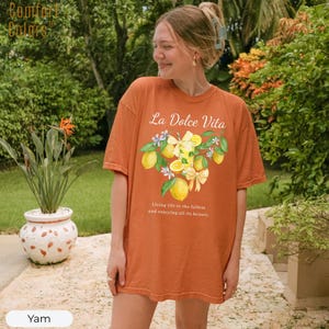 K&ouml;nnte beinhalten: Ein orangefarbenes T-Shirt mit dem Text "La Dolce Vita" und einer Zitronengrafik. Das Shirt hat auch den Text "Living life to the fullest and enjoying all its beauty." Das Shirt ist von der Marke Comfort Colors.