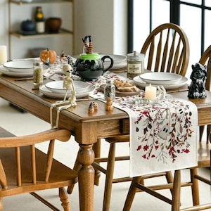 Puede incluir: Una mesa de comedor de madera decorada para una celebración de Halloween. La mesa está decorada con un corredor espeluznante, platos, un esqueleto, un caldero de bruja y otras decoraciones festivas. La mesa está rodeada de sillas de madera.