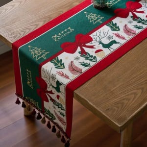 Puede incluir: Un camino de mesa navideño con un diseño verde y rojo. Presenta el texto "Merry Christmas", lazos rojos, árboles de Navidad y motivos de renos. Los bordes están adornados con borlas.