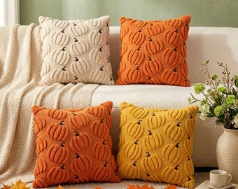 May include: Four square throw pillows featuring a raised, textured pumpkin pattern. The set includes one cream, one orange, one burnt orange, and one yellow pillow, each with a repeating motif of pumpkins across the entire front surface.