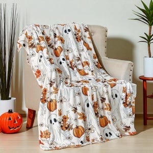 May include: A white Halloween-themed throw blanket draped over a chair. The blanket features a repeating pattern of friendly ghost figures, pumpkins, and floral elements in orange and brown. The blanket is made of a soft material.