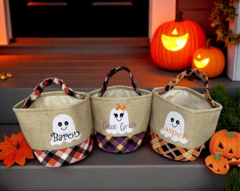 Puede incluir: Tres bolsas de golosinas de Halloween con diseños de fantasmas y nombres personalizados: Baron, Chloe Grace y Jasper. Las bolsas tienen fondos y asas a cuadros, con calabazas iluminadas en el fondo. Las bolsas son beige con diseños de fantasmas blancos.