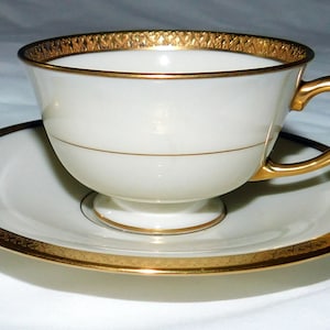 May include: A white teacup and saucer with a gold rim and a gold band around the middle of the cup.