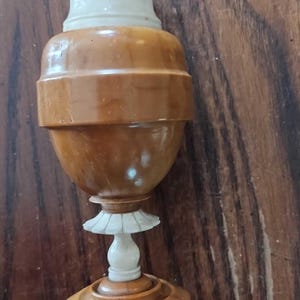 May include: A wooden vase with a white ivory top and base. The vase has a round body with a decorative band around the middle. The base is a round disc with a raised edge.