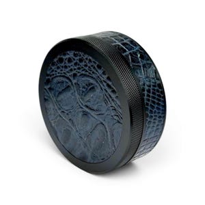 May include: A round, black grinder with a textured, dark blue, crocodile-skin pattern on the top and bottom. The side band is black with a textured, ridged design. The grinder is set against a white background.