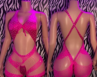 May include: A vibrant pink bodysuit with a halter neck, cut-out design, and rhinestone detailing. The shorts section has a fishnet pattern. The back features criss-cross straps and rhinestone accents. The bodysuit is displayed on a mannequin.