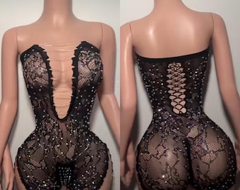 Könnte beinhalten: Schwarzer Spitzen-Overall mit trägerlosem Design und tiefem V-Ausschnitt. Der Overall ist mit funkelnden Strasssteinen verziert und hat einen Rücken im Korsett-Stil. Der kurze Teil hat eine taillierte Silhouette.