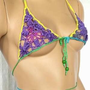 May include: A handmade crochet bikini set in shades of purple, yellow, green, and teal. The top features a floral design with a halter neck, and the bottoms are a thong style. The bikini is tied with string.