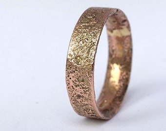 Op de afbeelding: Een getextureerde gouden en koperen trouwring met een gehamerde afwerking.