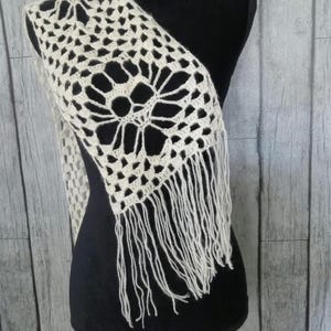 May include: A white crocheted scarf with a fringe. The scarf has a delicate floral pattern.