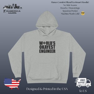 May include: A light grey hoodie featuring the text "WORLD'S OKAYEST ENGINEER" in black. The hoodie has a hood with drawstrings and a spacious pocket. The image also includes the text "Designed & Printed in the USA".