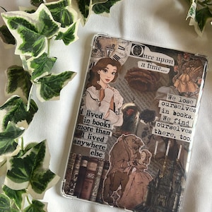 Puede incluir: Funda transparente para teléfono con un collage inspirado en "La Bella y la Bestia". El diseño incluye ilustraciones de Bella y la Bestia, además de texto como "Érase una vez..." y "Nos perdemos en los libros."