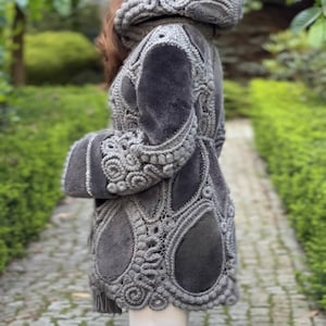 May include: A gray coat with a hood, featuring intricate crochet detailing. The coat has a plush, textured appearance with a tailored fit. The design includes floral and teardrop-shaped patterns, creating a unique and elegant look.